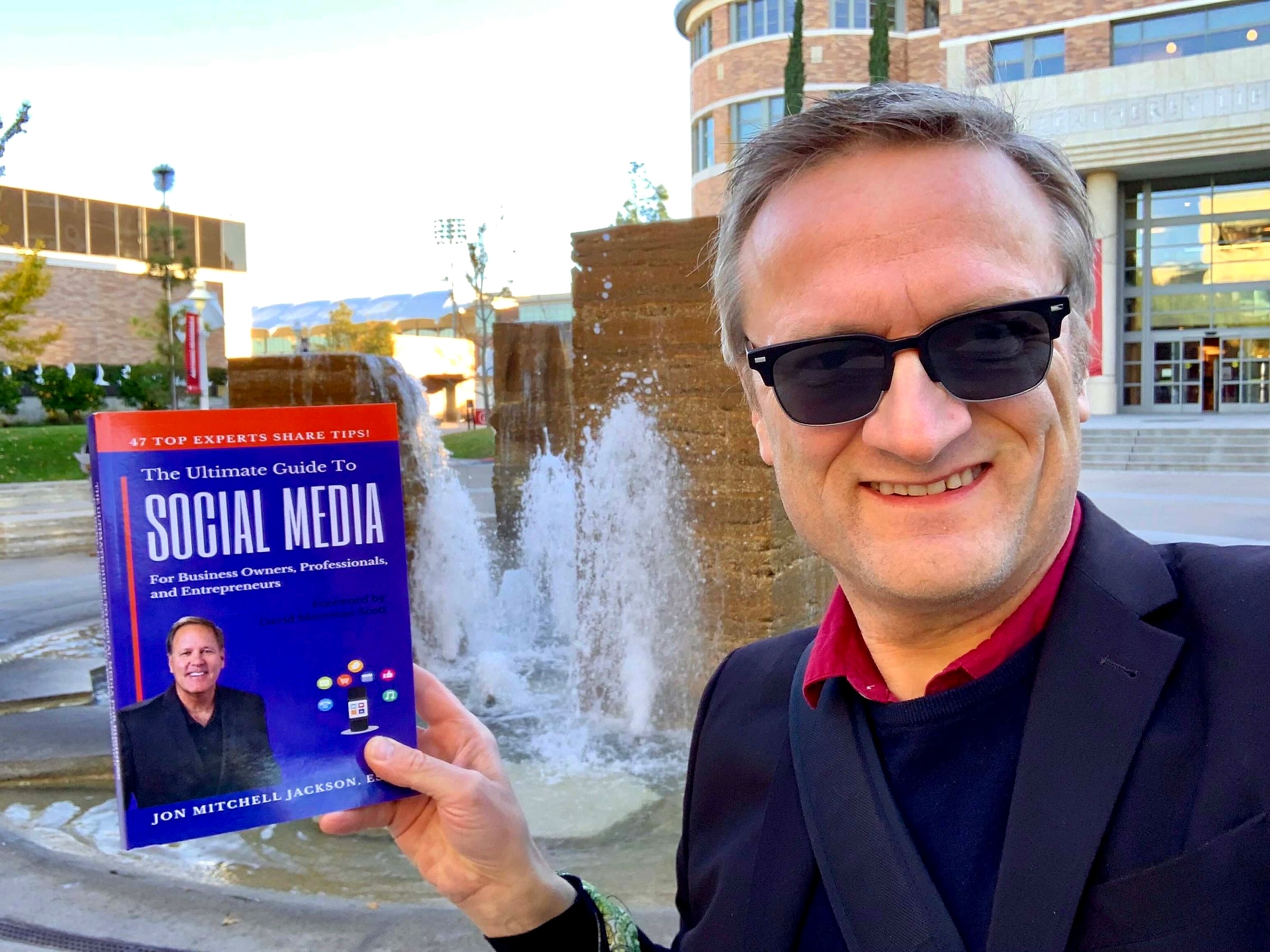 Niklas in sunglasses holding The Ultimate Guide to Social Media by a fountain