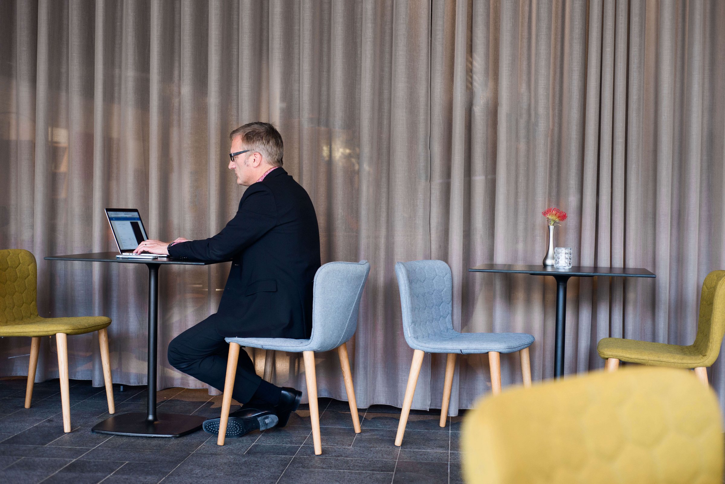 Niklas working at a small table in a hotel lounge with yellow and blue chairs
