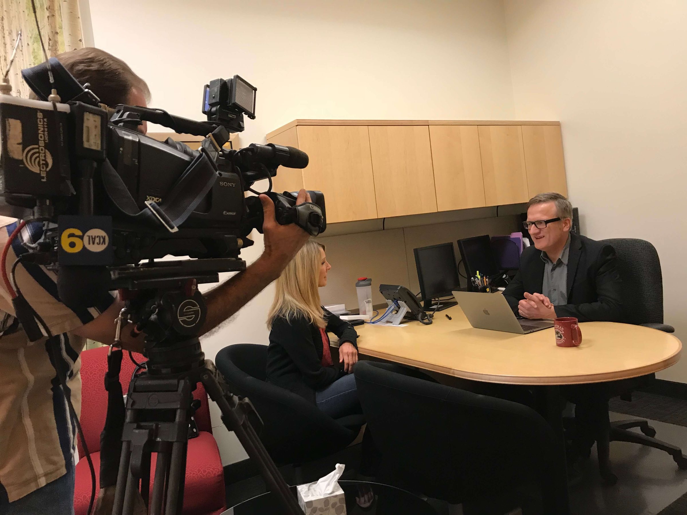 A CBS LA camera in the foreground, Niklas at his desk behind
