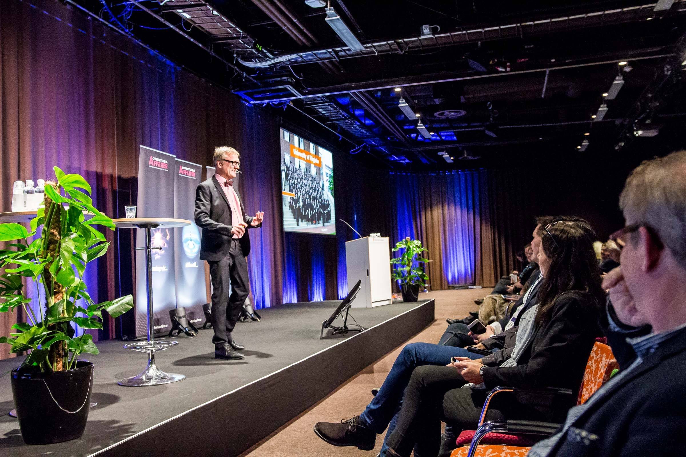Niklas presenting beside a tall plant and his slides, Stockholm