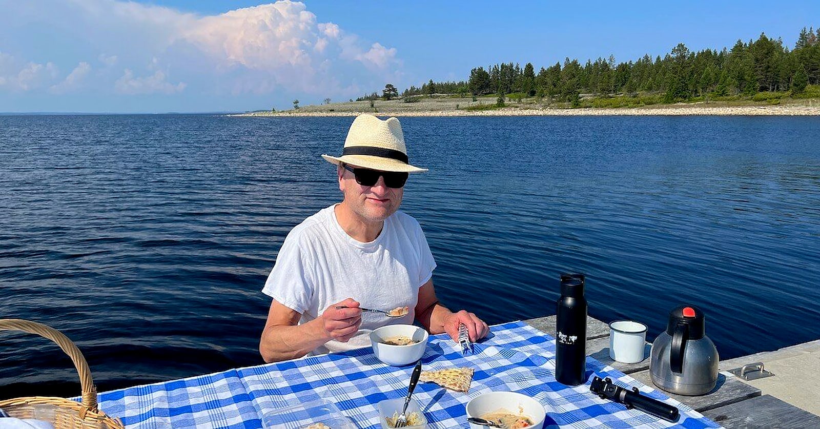 Niklas in a sun hat at a breakfast table by the water on Stenskär island, Piteå